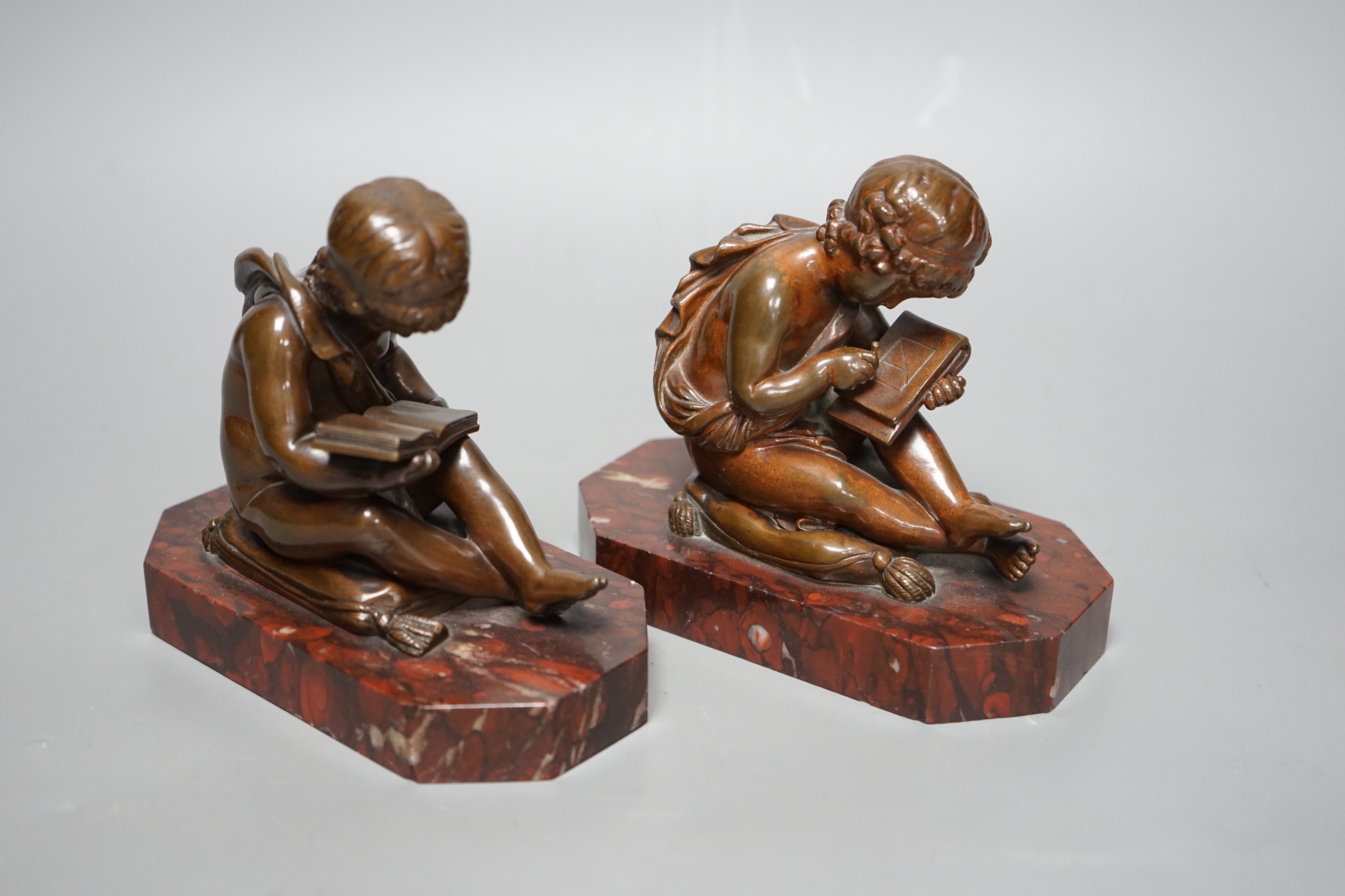 After Charles Gabriel Lemire (1741-1827), a pair of bronze studies of boys seated on cushions, writing and reading, E. Colin & Cie, Paris foundry marks, on rouge marble bases, 14cm long